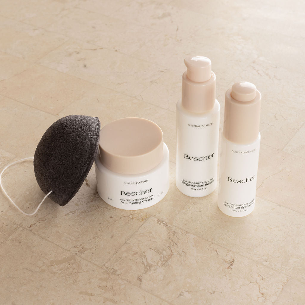 A skincare trio pack consisting of a jar, a serum bottle, and a cream bottle, with a Konjac sponge, all displayed on a marble surface.