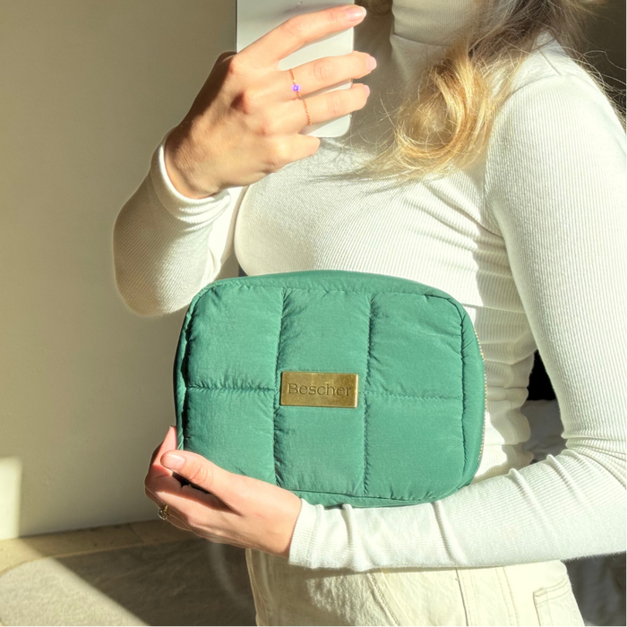 Person holding a green pouch with a brand label, taking a mirror selfie.