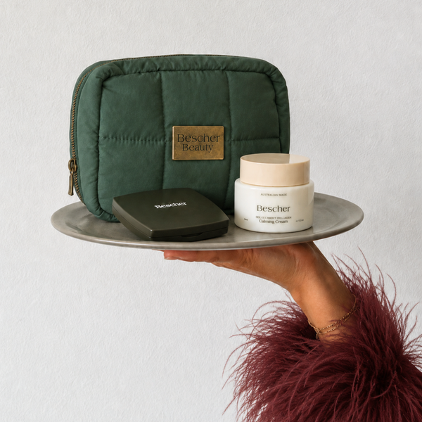 Hand holding a green cosmetic bag with Bescher products on a white background