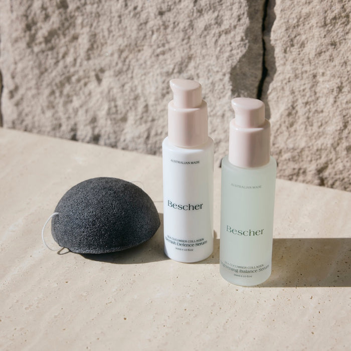 Two skincare bottles labeled 'Bescher' and a konjac sponge on a stone surface.