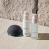 Two skincare bottles labeled 'Bescher' and a konjac sponge on a stone surface.