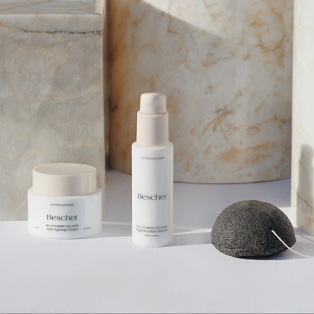 A skincare product duo with a face serum in a white pump bottle and a face cream jar, placed on a marble surface next to a konjac sponge.